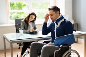 Man in a wheelchair with a cast on his arm looks distressed as he's in a meeting with a professional