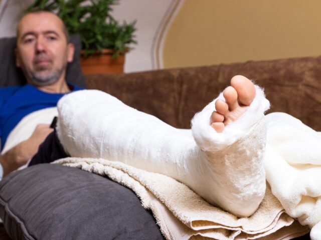 Man with a cast on his foot laying in bed in pain